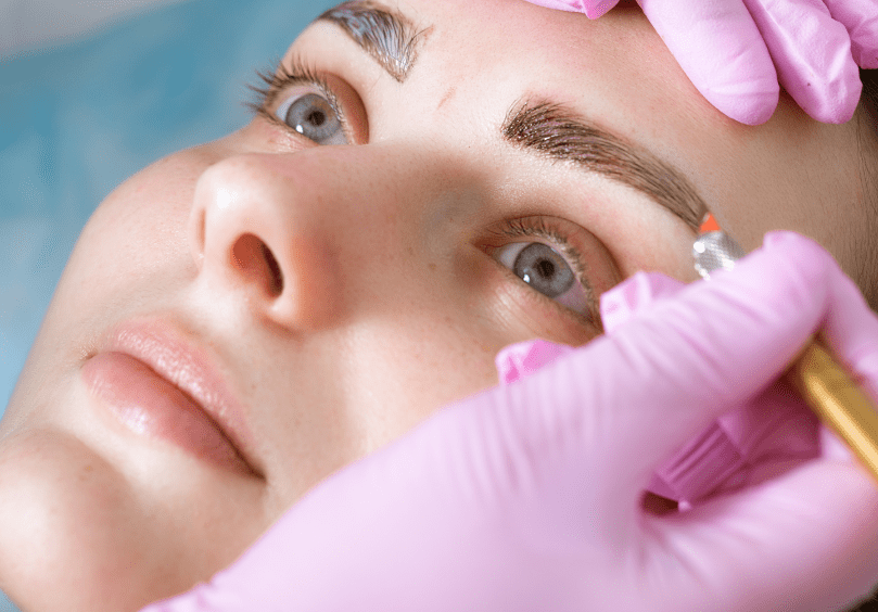 A woman getting her eyebrows tattooed with pink gloves.