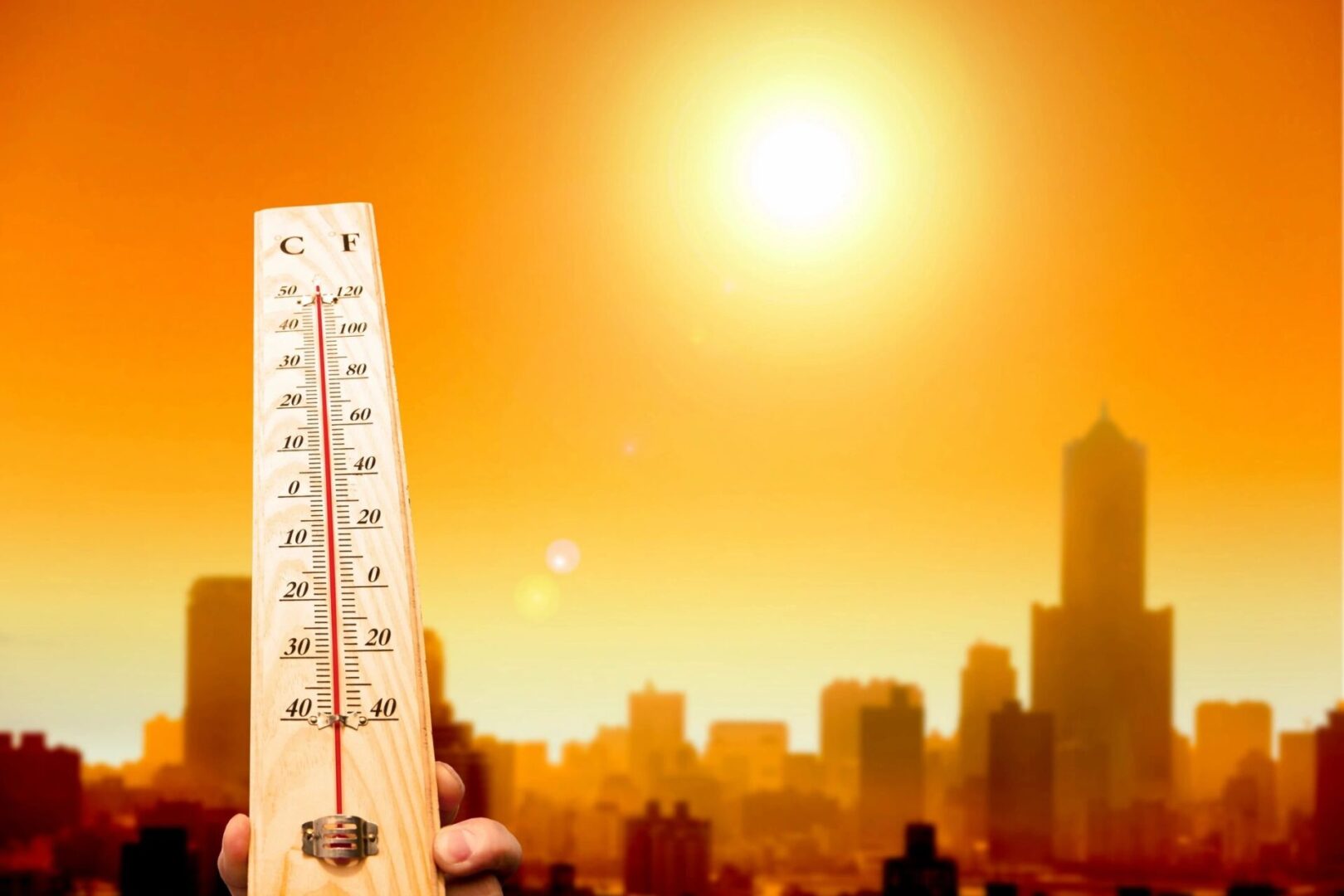 A thermometer in front of the sun with a city skyline behind it.